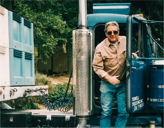 Old photo of Founder, Dan Smith, stepping out of a blue semi truck with bins of grapes.