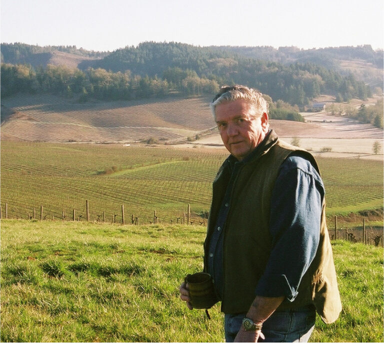 Founder, Dan Smith, holding a cup of coffee, overlooking the vineyard.