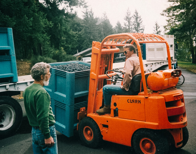 Founder, Dan Smith on orange tractor talking to a man while unloading grapes on bins.