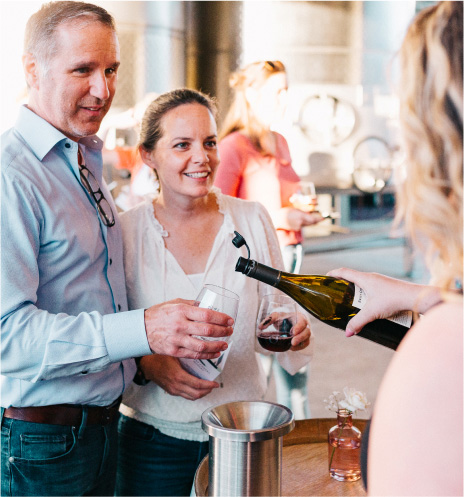Man and woman holding out glasses for wine sample at an event.