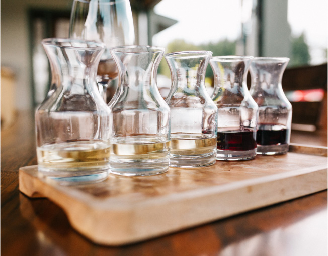 Wooden flight tray with five samples of wine in small glass carafes.