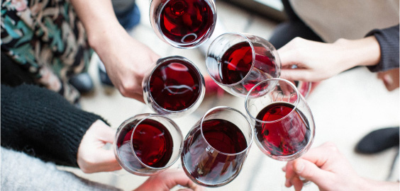 Six hands cheering glasses of red wine together.
