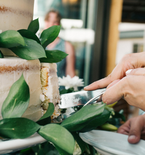Hand cutting into a two-tiered cake, decorated with leaves.