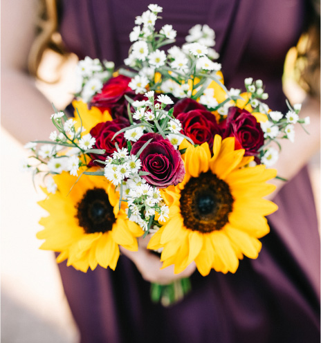 Woman holding a boquet of sunflowers and roses at a wedding. 