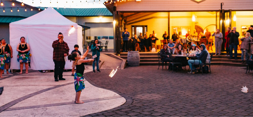 Girl dancing on the patio at an event in the evening with string lights over the patio and other people watching her.